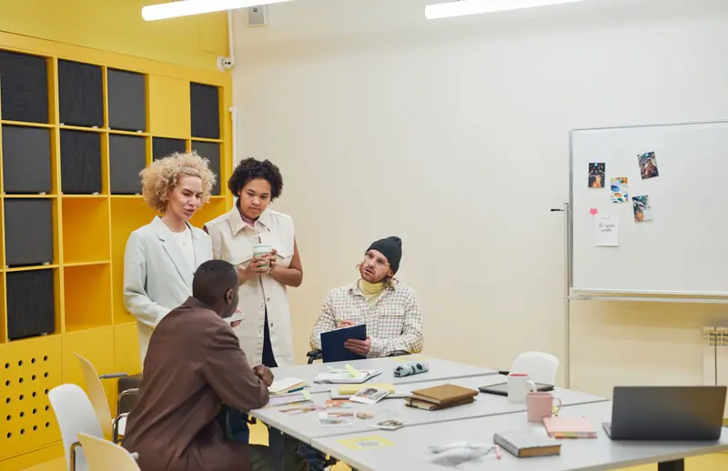 Voksne som samarbeider og diskuterer rundt et bord i et lyst rom med gule vegger